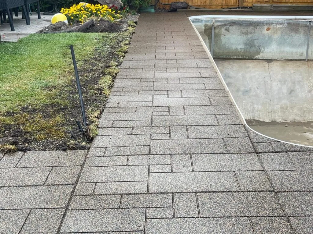 a brick interlocking walkway with a pool in the back
